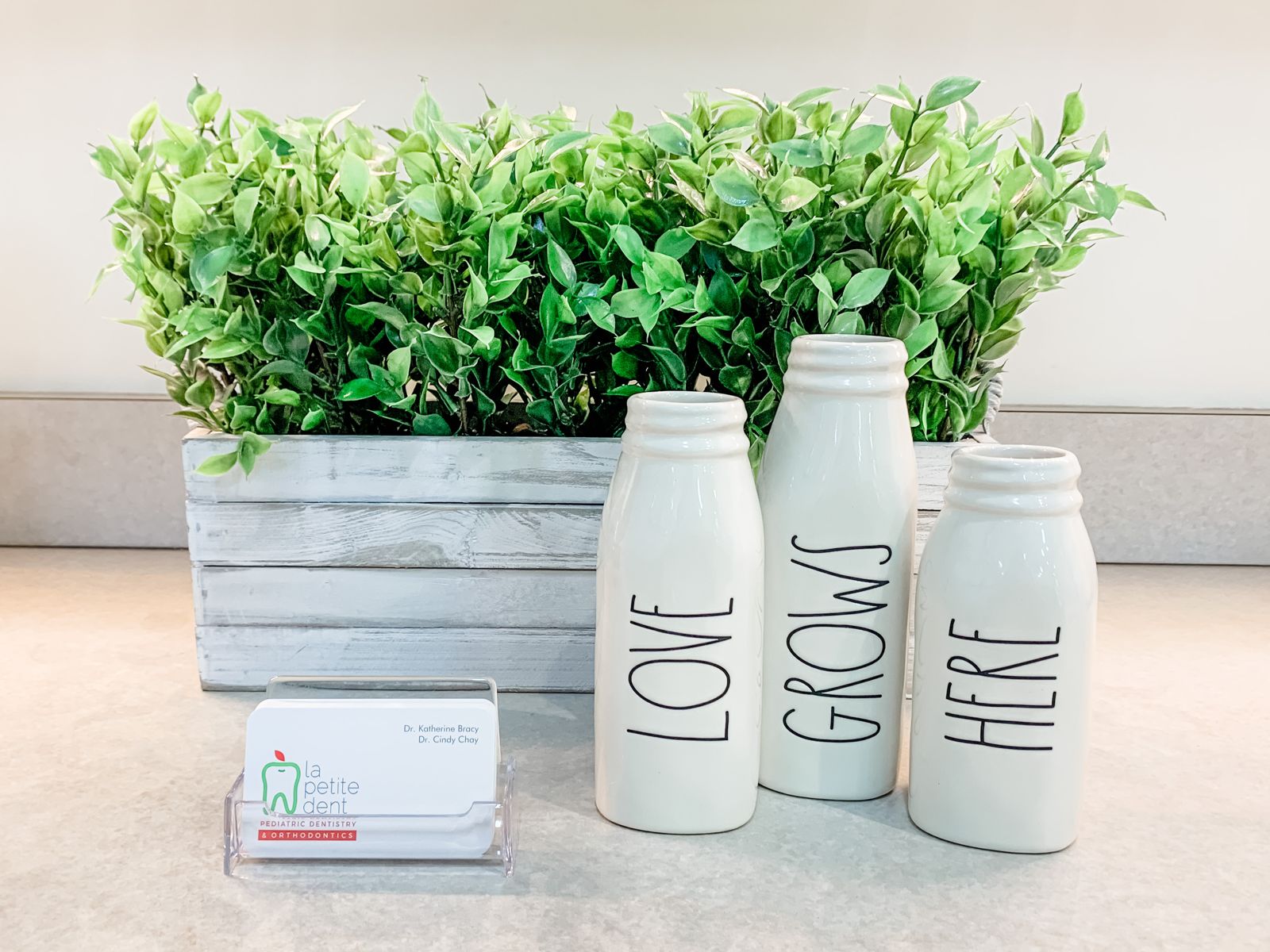 Milk-bottle vases in the La Petite Dent office spelling Love Grows Here, beside the practice's business card