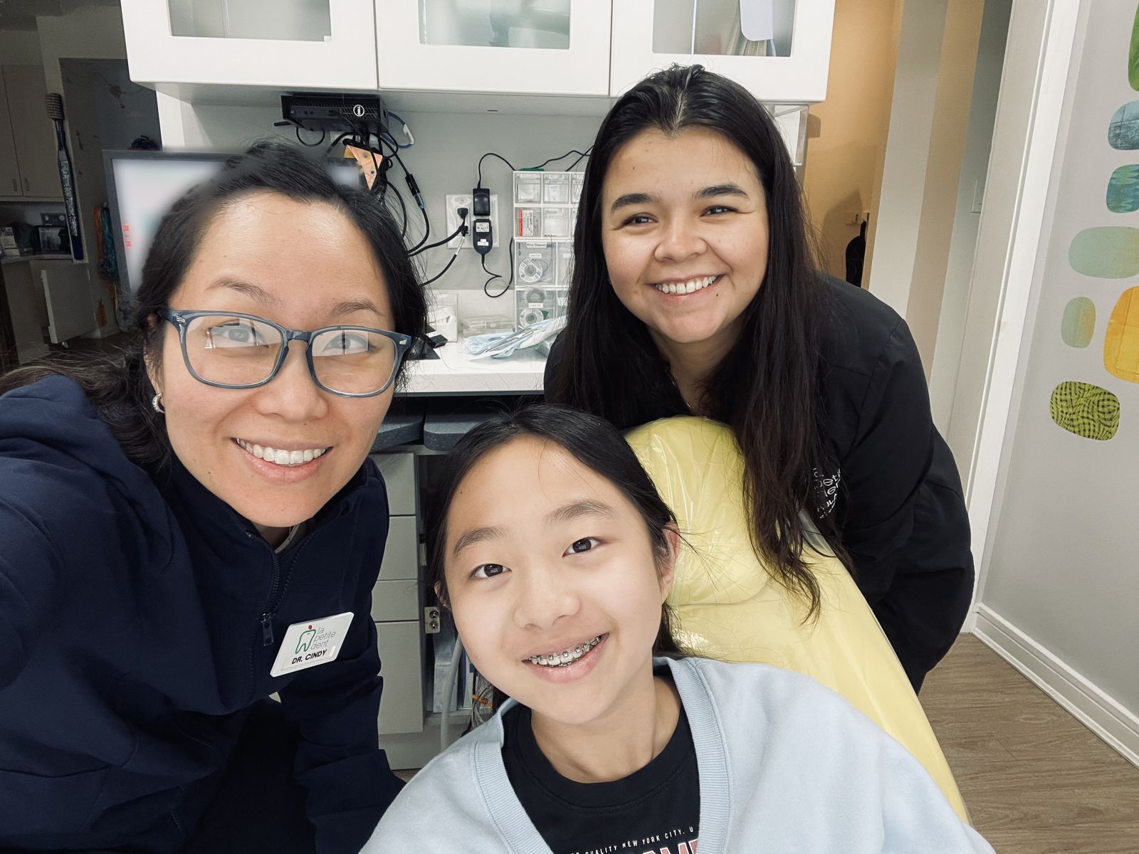 Dr. Cindy smiling with her daughter, who is wearing braces, and a member of the orthodontic team