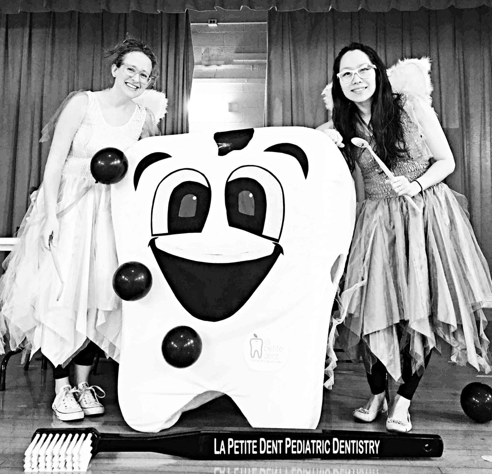 Dr. Bracy and Dr. Cindy dressed as tooth fairies, standing beside a giant smiling tooth and a giant toothbrush