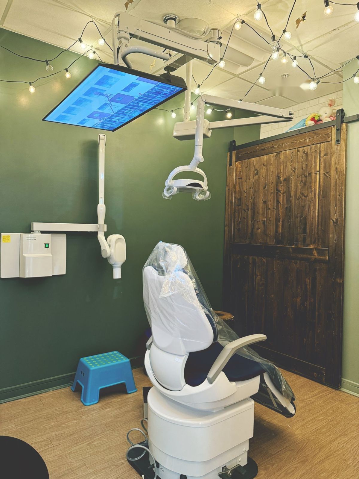 A treatment room with green walls, string lights, a barn door, and a TV on the ceiling
